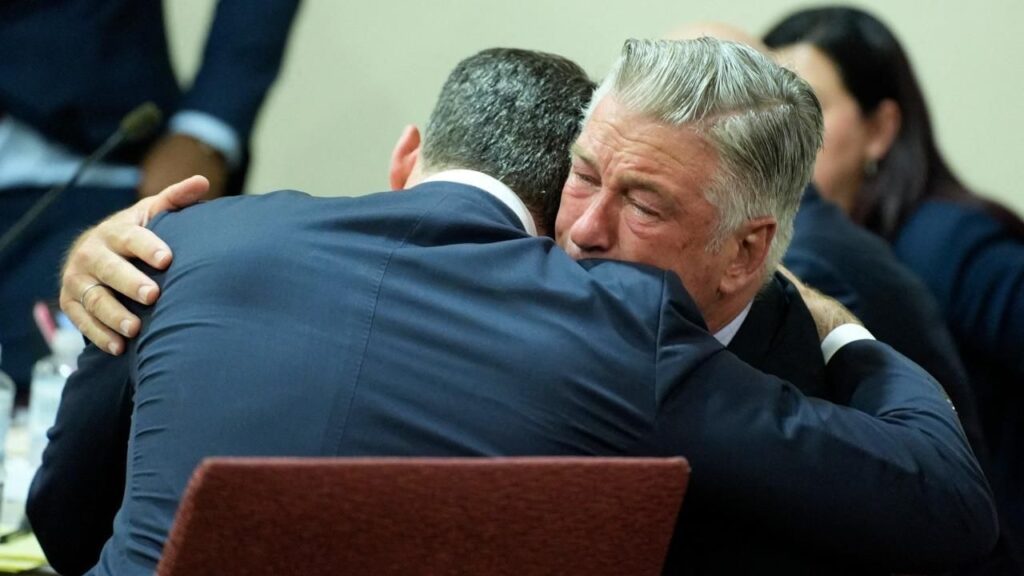 Alec Baldwin hugging another man tearyeyed