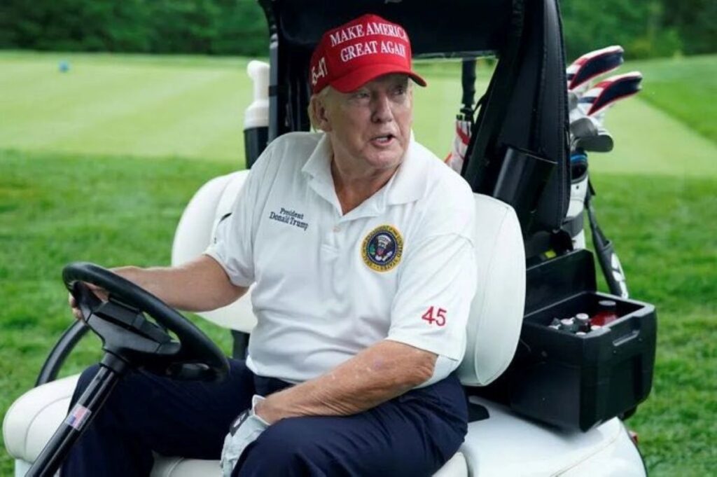 Donald Trump in golf ensemble seated in a golf cart