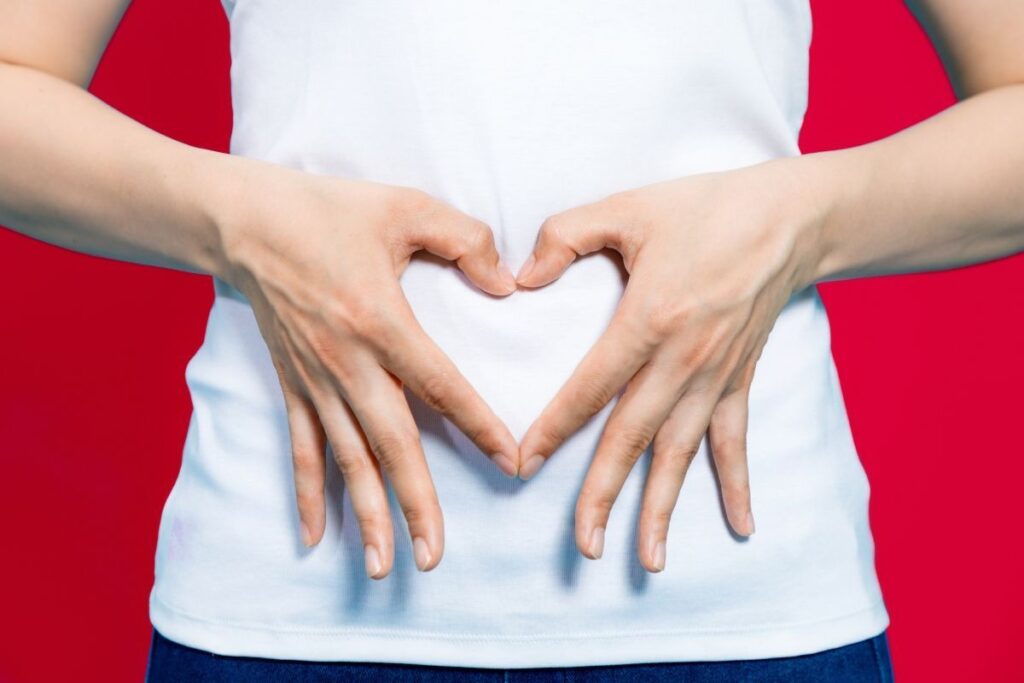 A woman making the heart shape with her hands on her belly